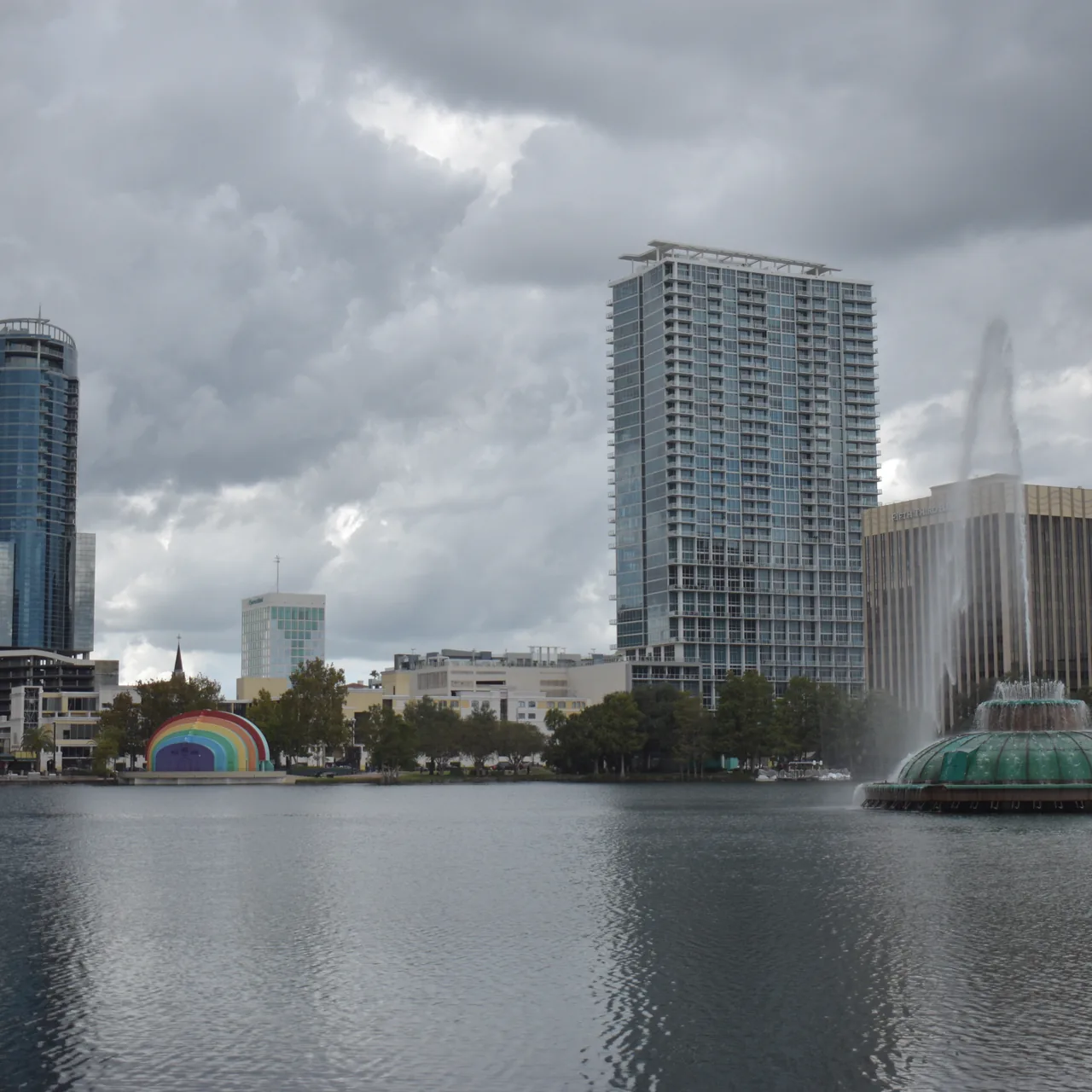 Lake Eola Park with Orlando downtown skyline, the green glass Linton Allen fountain, and the rainbow Walt Disney Amphitheater bandshell